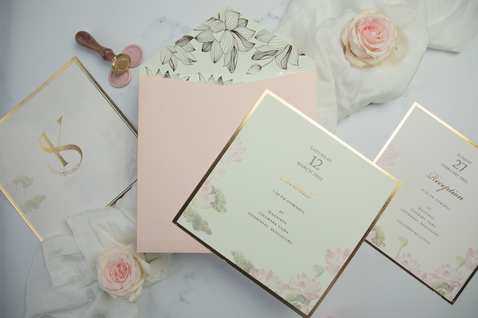 Gold-foil cocktail and reception cards with lotus artwork, a monogram card, a peach envelope and a wax seal