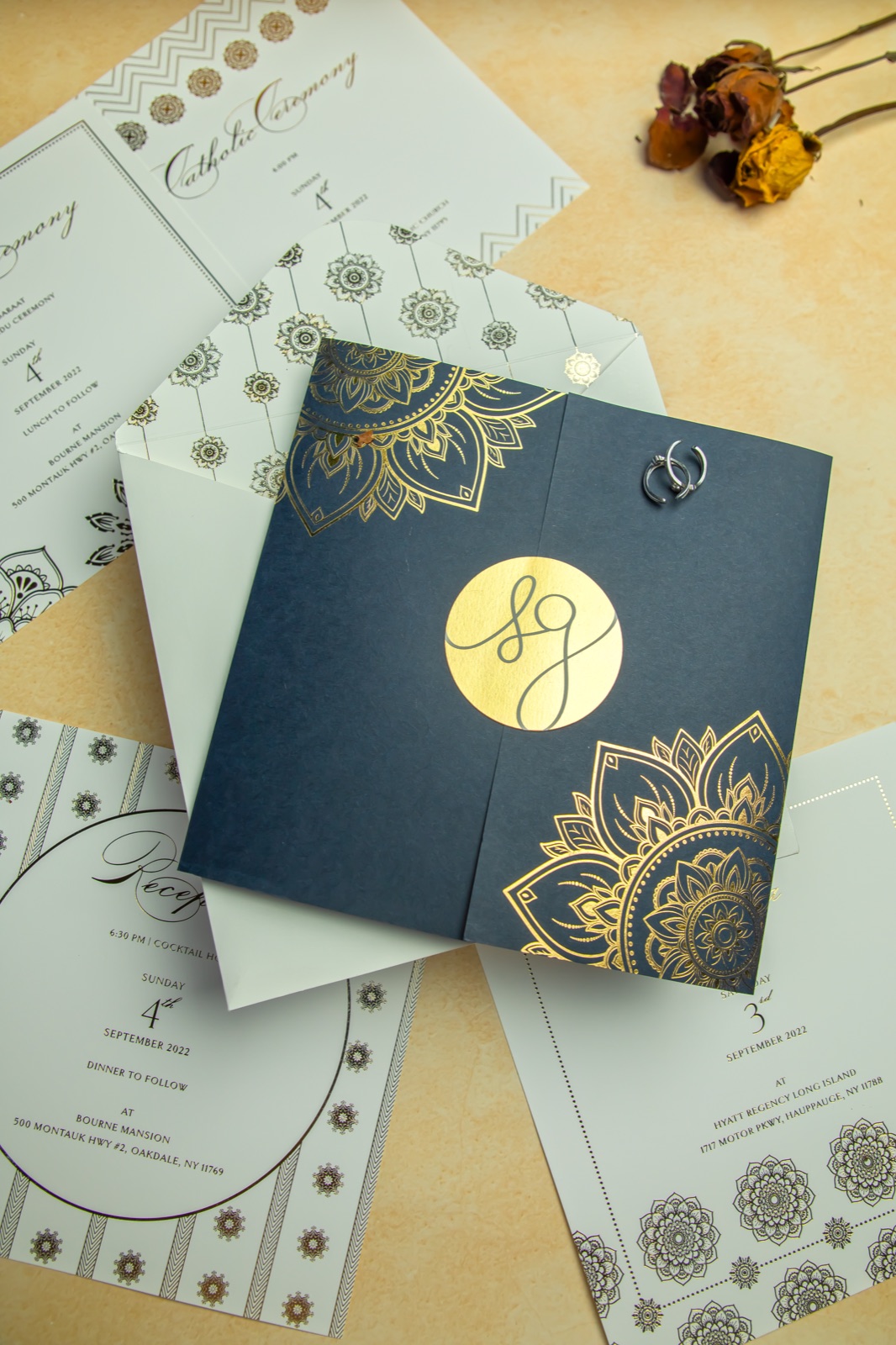 Navy gatefold invitation with gold-foil mandalas and a gold monogram, laid over ceremony and reception cards