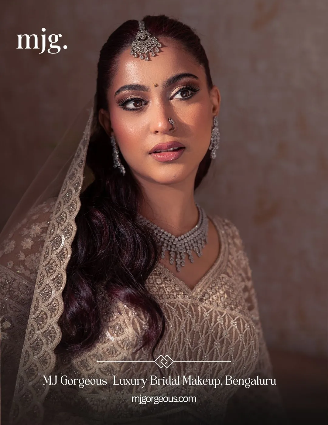 Bride in soft glam makeup with an ivory embellished lehenga, a veil, bridal jewellery and loose side-swept waves