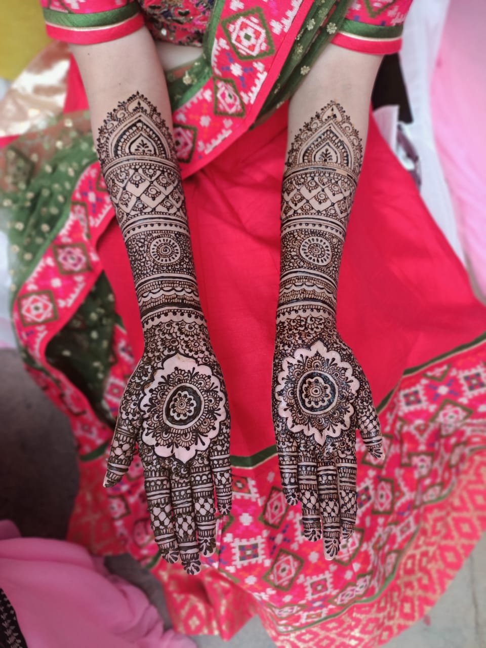 Bridal mehendi on both palms and forearms, with a large mandala in the centre of each palm and banded patterns to below the elbow