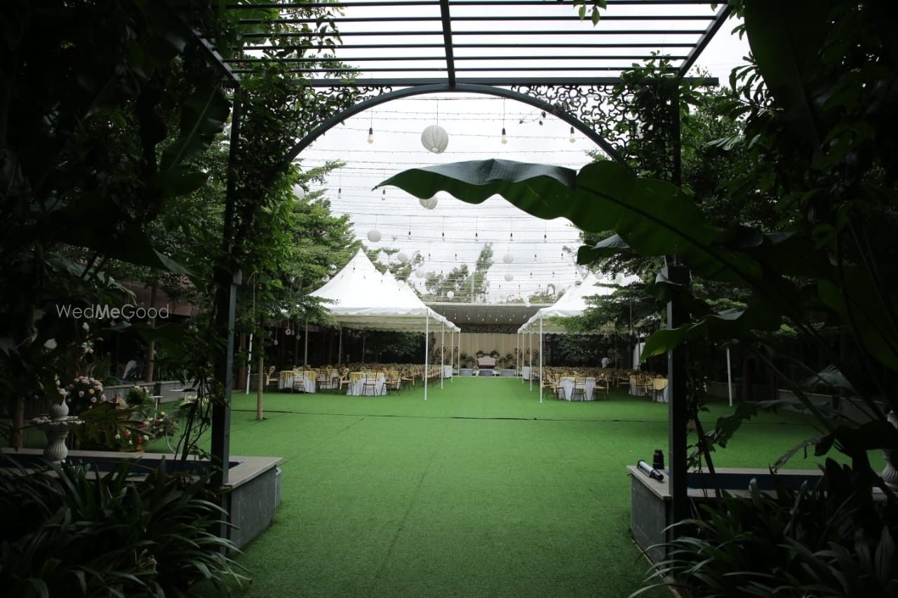 Covered gallery at Aarambha looking out to the lawn, with a pergola frame, hanging globe lights and tables set under a marquee beyond