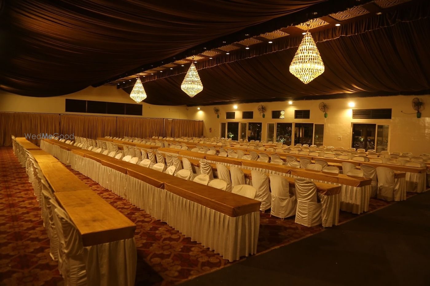 Banquet Hall 2 at Aarambha with a dark draped ceiling, crystal drop chandeliers and long banqueting tables in gold running the length of the room