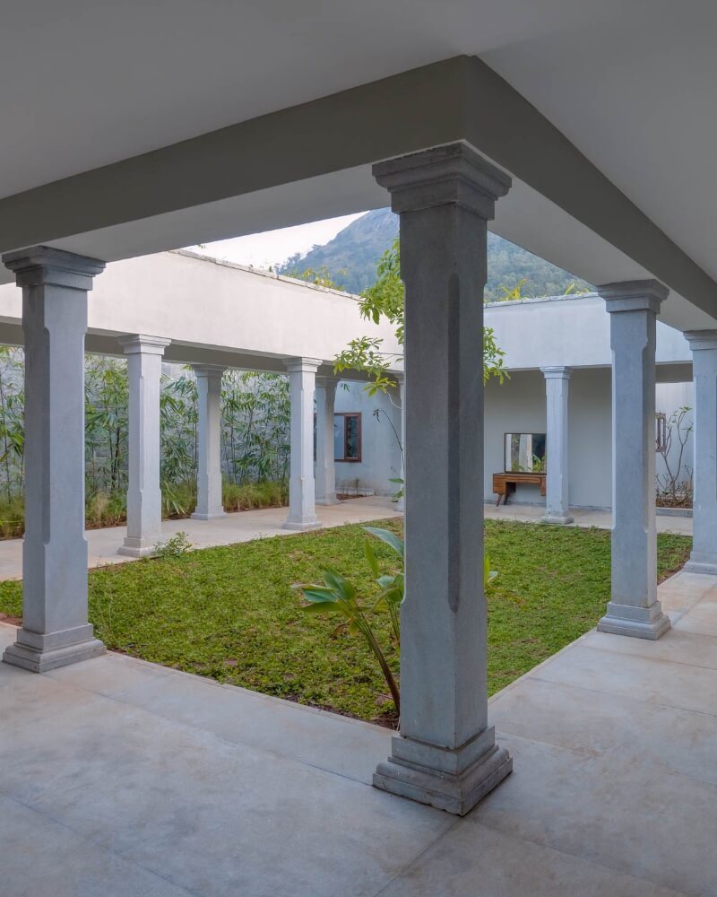 The courtyard of one of the two villas at Amita Rasa — a square of lawn enclosed by a granite colonnade and covered walkway, a young tree at its centre, bamboo against the far wall and the Nandi hillside visible over the roof