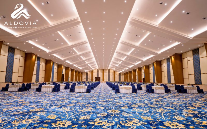 The Ocean convention hall at Aldovia set end to end with round tables in cream cloths and navy chair covers, receding down a very long pillar-less room with a coffered white ceiling, timber and blue wall panels and a blue-and-gold patterned carpet