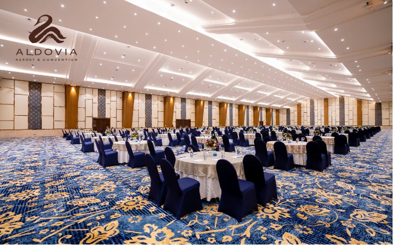 The Ocean hall at Aldovia from one corner, set with navy-covered chairs at cream round tables under a starlight-pinhole ceiling, with folding timber partitions and blue upholstered panels along the side wall