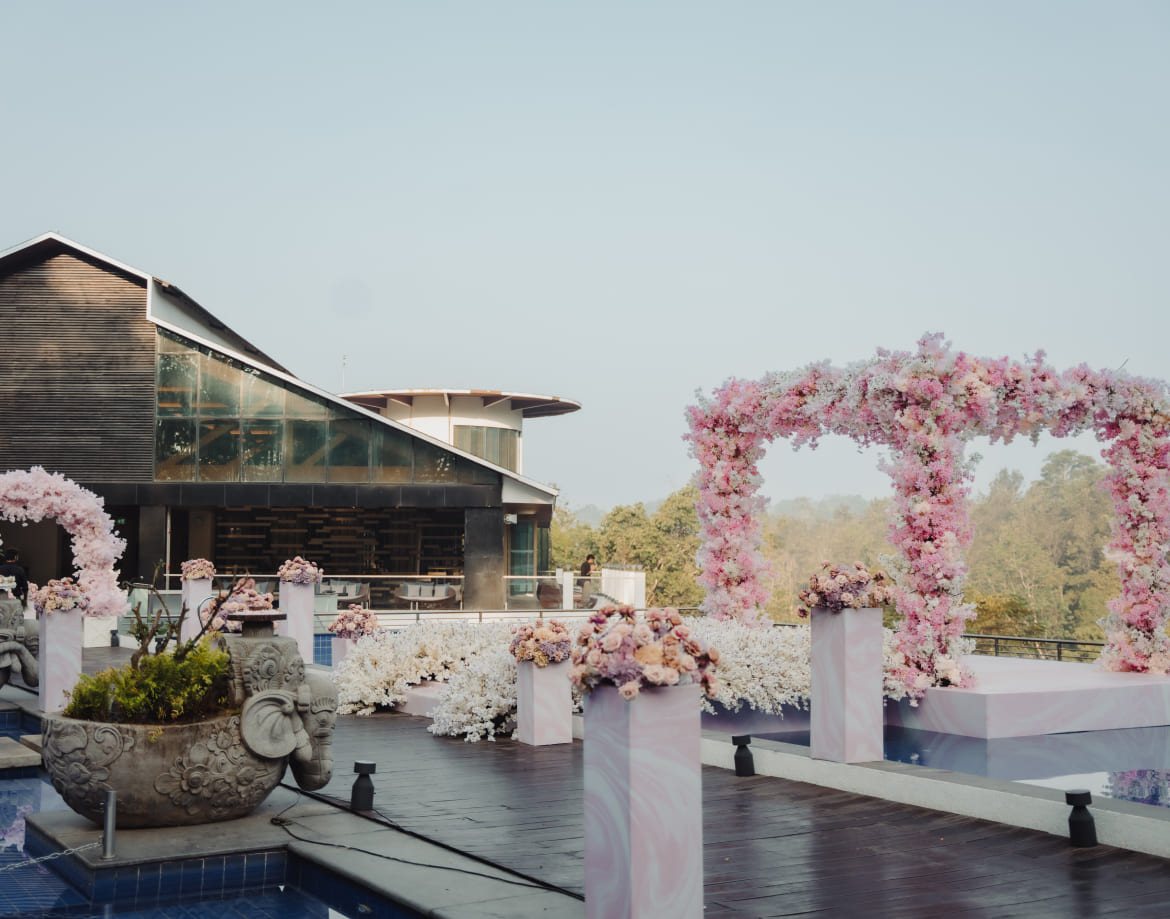 Poolside ceremony set-up at Coorg Marriott with a blossom arch and white floral banks, the resort's glass and timber block on the left