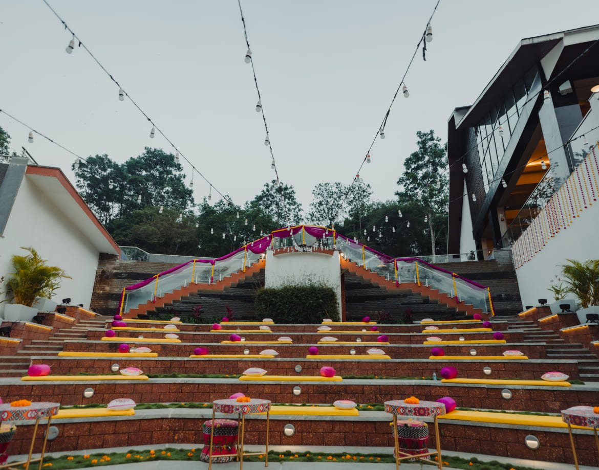 The stepped terraces at Coorg Marriott dressed for a daytime function with yellow mattresses, bolsters and low tables, festoon lighting strung overhead