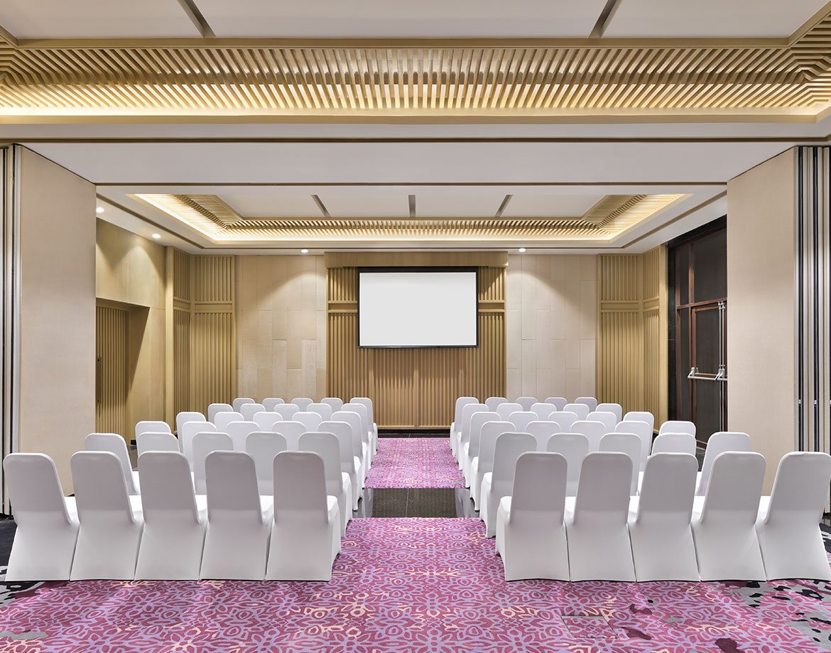 The air-conditioned banquet room at Coorg Marriott in a narrower theatre layout, patterned carpet and a lit cove ceiling
