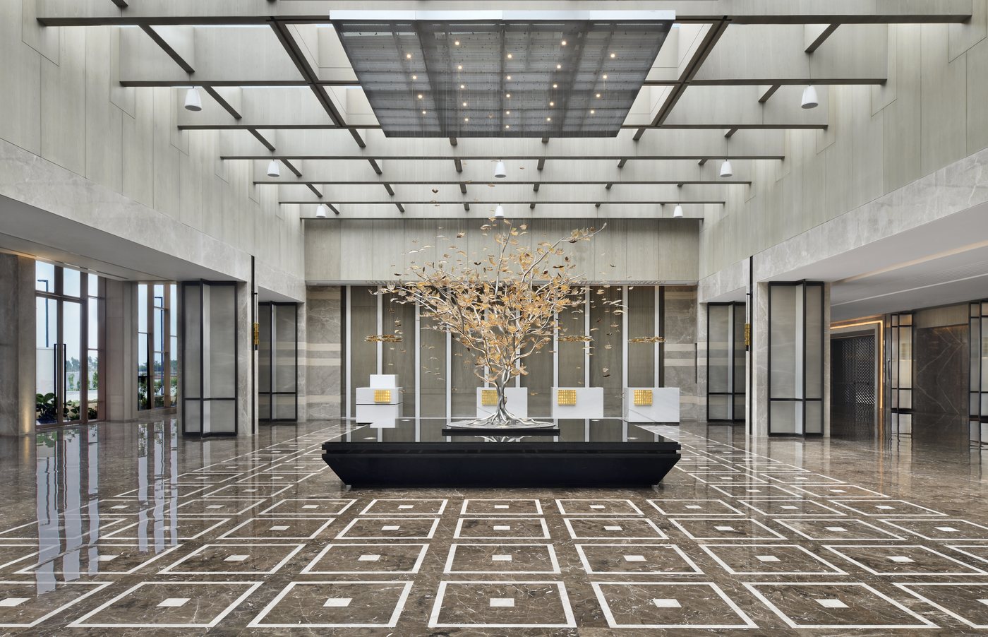 The double-height pre-function foyer of the Convention Centre — polished patterned marble floor, a gilded metal tree sculpture on a black plinth as the centrepiece, and a deep coffered ceiling grid with a lit skylight panel above