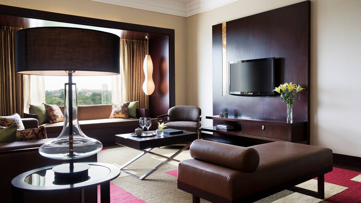 A suite living room at JW Marriott Bengaluru with dark timber panelling, a window seat and a view over the Cubbon Park tree line