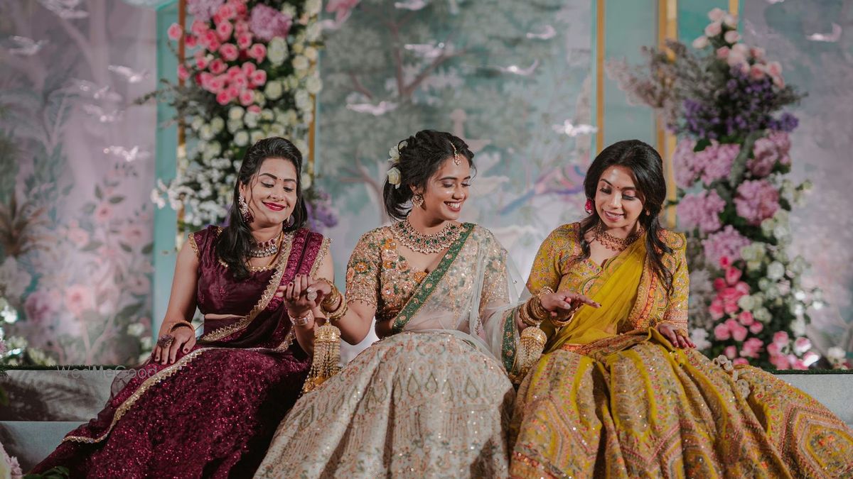 A sangeet stage at Kochi Marriott Hotel — pastel botanical backdrop panels edged with pink and white roses, three guests in embroidered lehengas seated at the front