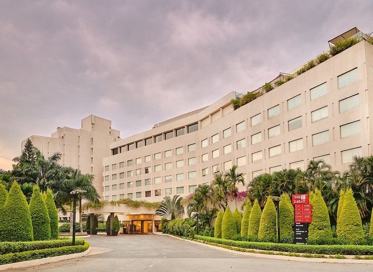 The LaLiT Ashok Bangalore exterior at dusk — the long stepped block behind a topiary-lined driveway and porte cochère