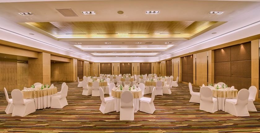 The Grand Ballroom at The LaLiT Ashok Bangalore in round-table banquet layout with cream covers under a lit cove ceiling