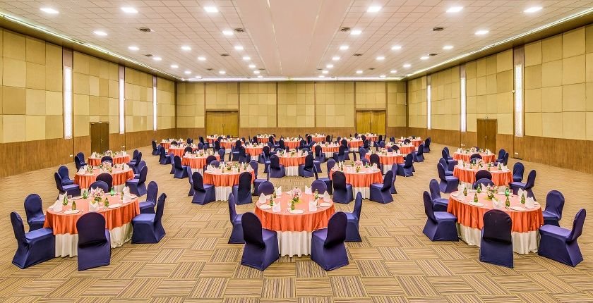 Kalinga banquet hall at The LaLiT Ashok Bangalore laid with round tables in orange and blue linen across an open pillar-less floor