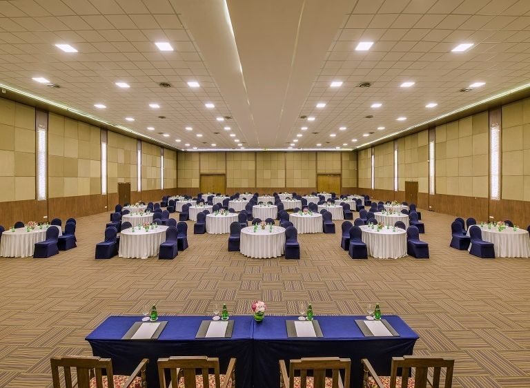 Wider view of Kalinga at The LaLiT Ashok Bangalore, round tables in blue and white filling the column-free floor with a long head table in front