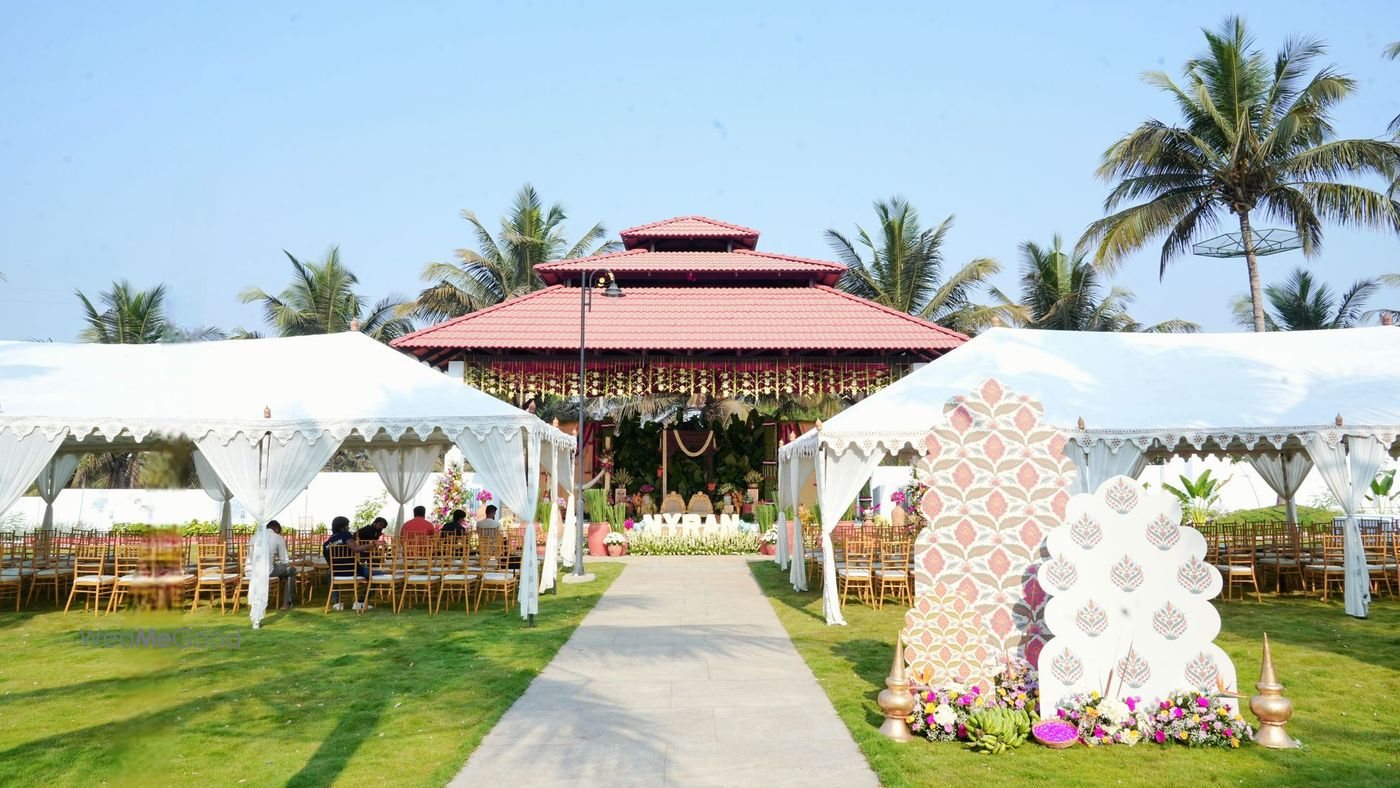 The main lawn at Mandara in daylight — white canopy tents either side of a paved path leading to the open pagoda-roof pavilion, with palms along the boundary