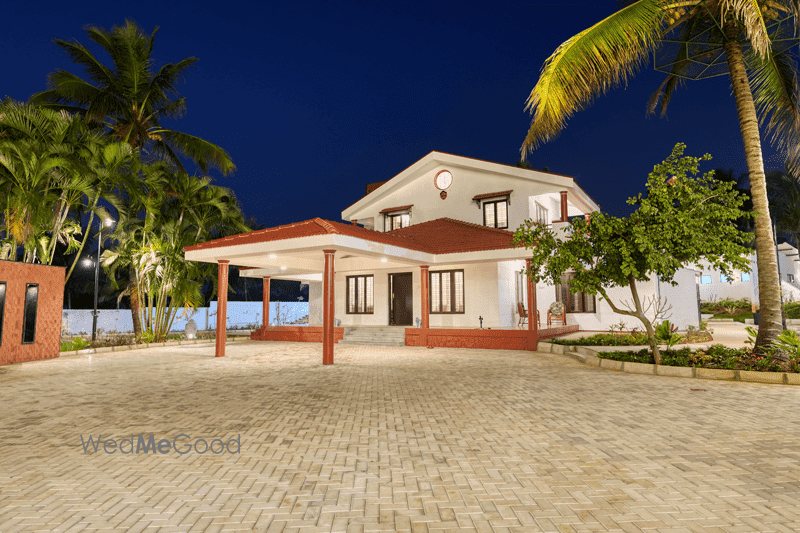 The white portico house at Mandara lit at night above a broad paved forecourt, with palms and lawn on either side