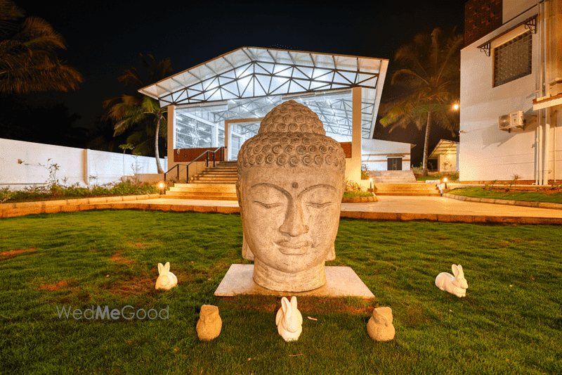 A large stone Buddha head sculpture lit on the lawn at Mandara at night, with a lit glazed structure and steps behind it