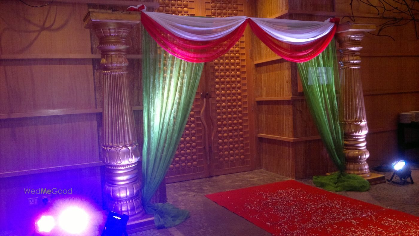 A dressed entrance at Bengaluru Marriott Whitefield — pink and green draped columns forming a threshold over a red carpet, lit from the floor against a timber screen wall