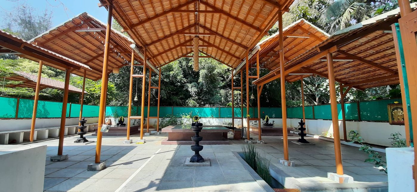 The open-air mantapa at MG Magnus: three pitched Mangalore-tile roofs on orange timber posts over a granite floor, with a raised red-granite homa platform and standing black lamp columns
