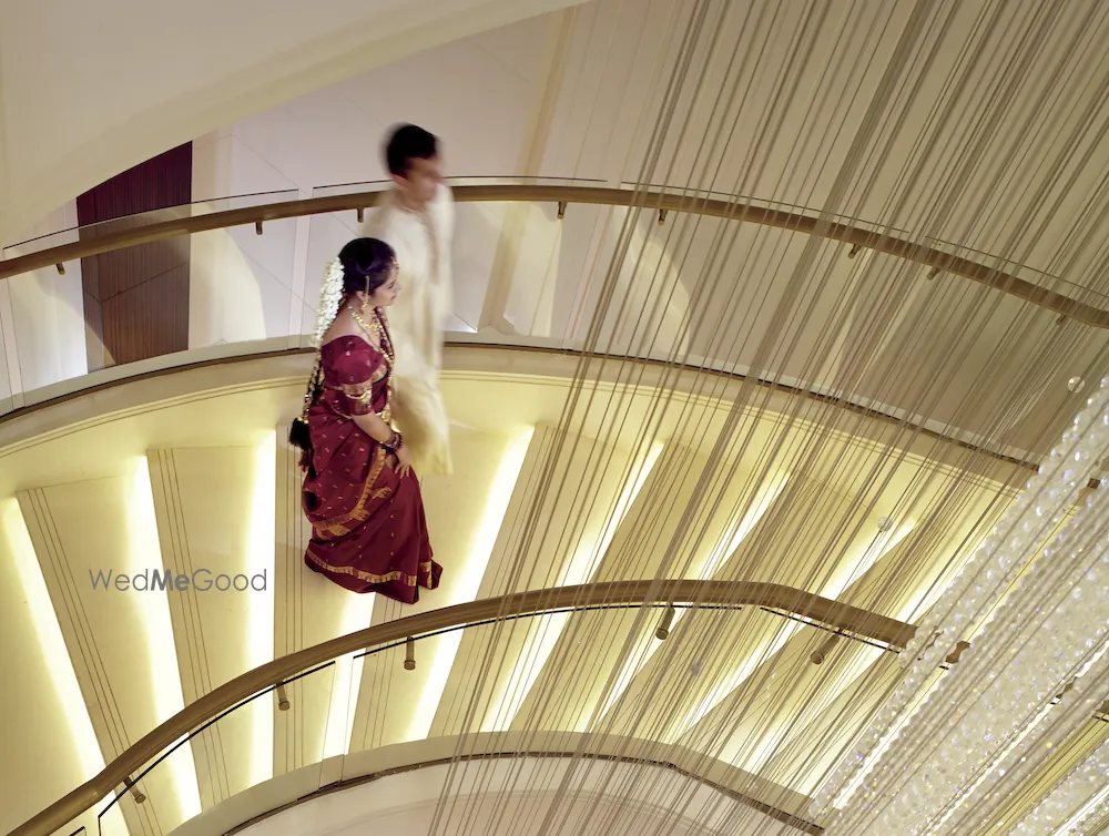 A couple walking down the curved staircase above the ballroom at The Ritz-Carlton Bangalore, seen through the strands of the crystal chandelier