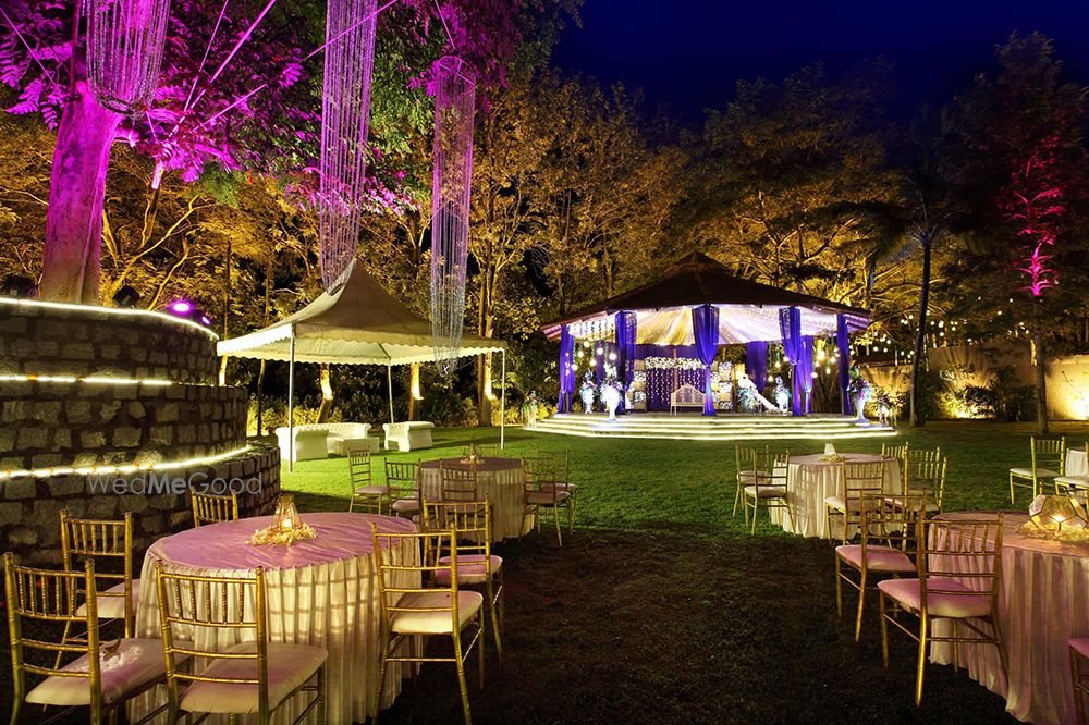Night reception on the Royalton Leisure lawn — round tables with gold chiavari chairs, a lit mandap pavilion and amber and magenta uplighting through the trees