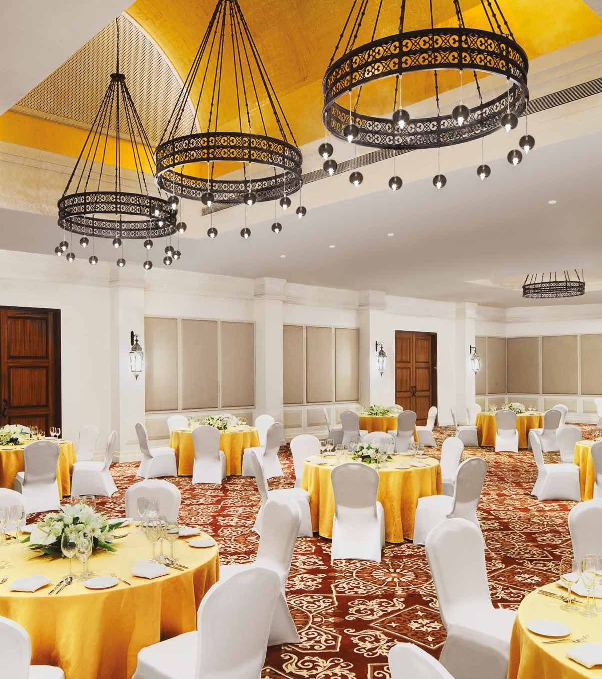 Soiree banquet hall at Taj Bekal set with round tables in yellow linen under cane-and-iron chandeliers, patterned carpet across the floor