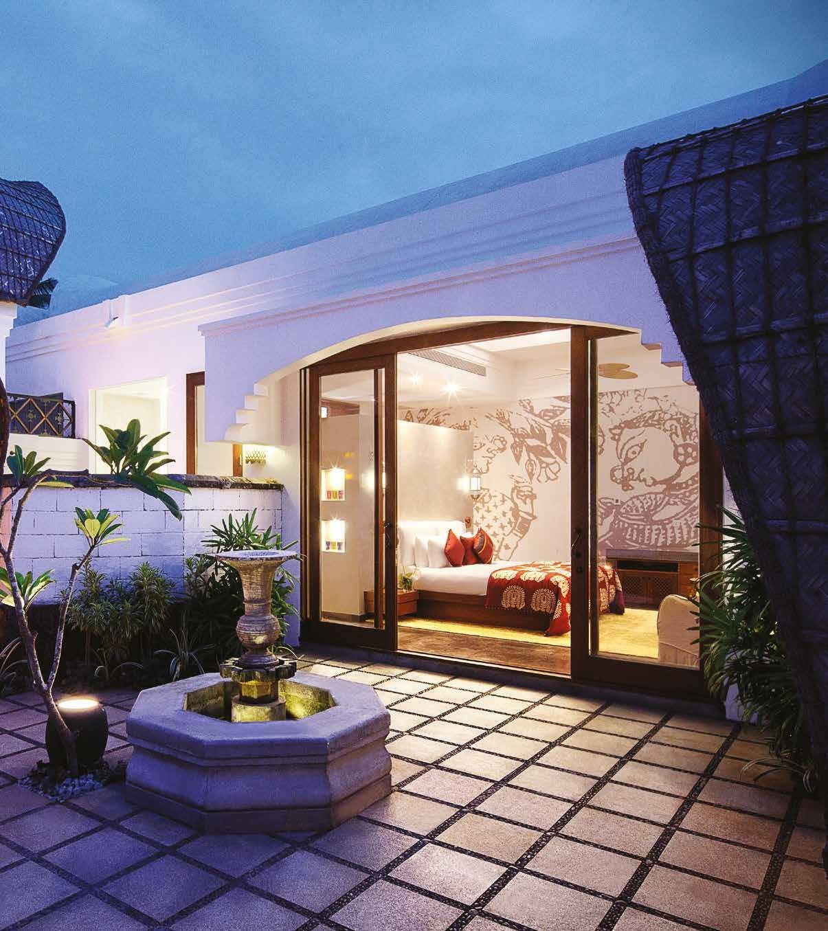 Villa courtyard at Taj Bekal at dusk with a stone water feature and the bedroom beyond, its wall carrying Chitra Pothi mural work