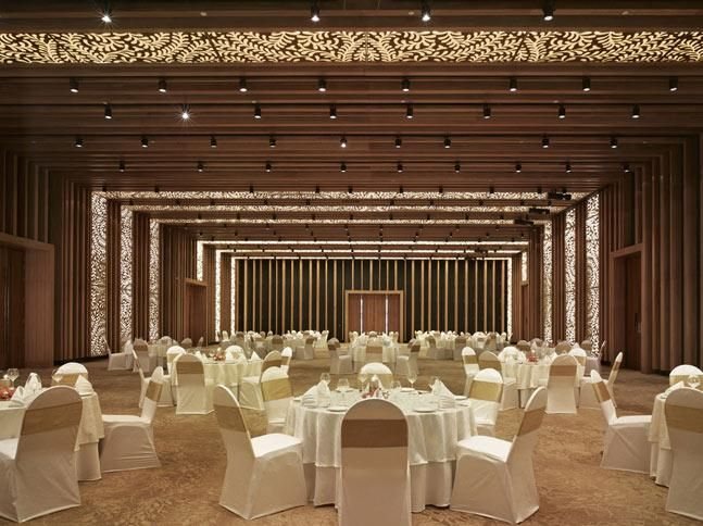 A banquet room at Taj Yeshwantpur laid for a seated dinner — round tables in white linen inside a hall lined with backlit perforated gold screens