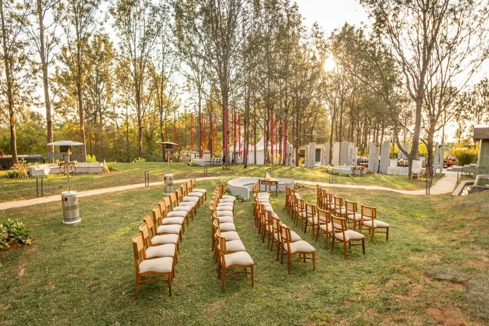 Curved rows of ceremony seating under the trees on the Aakasam lawn