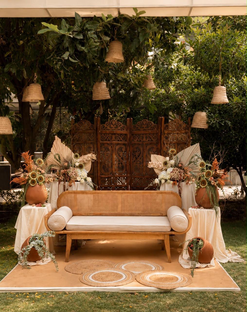 Boho mehendi seating with cane bench, carved wooden screens and cane bell lanterns in the trees at Ramada Yelahanka Bangalore