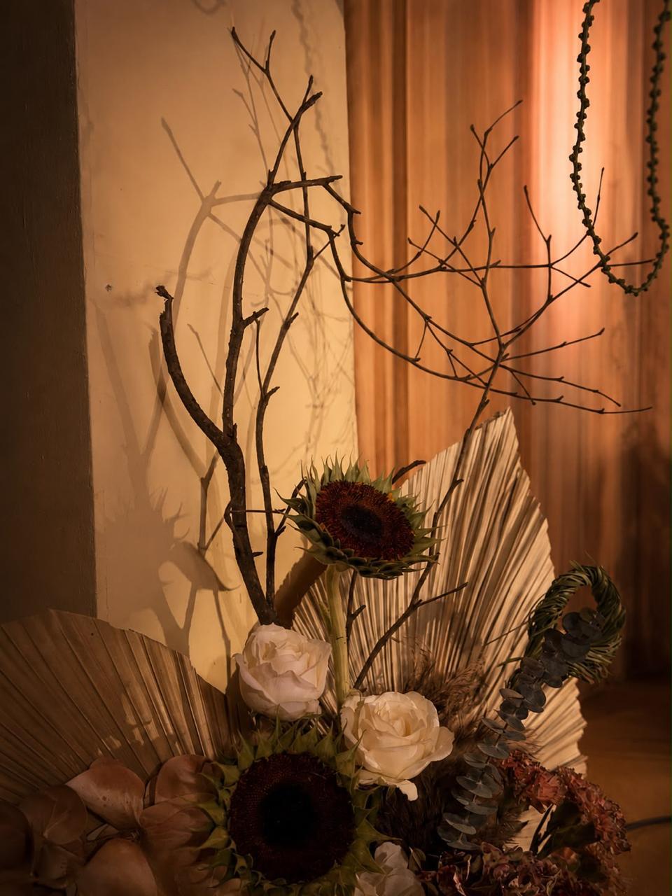 Sculptural arrangement of bare branches, sunflowers, white roses and dried palm at a boho wedding in Bangalore