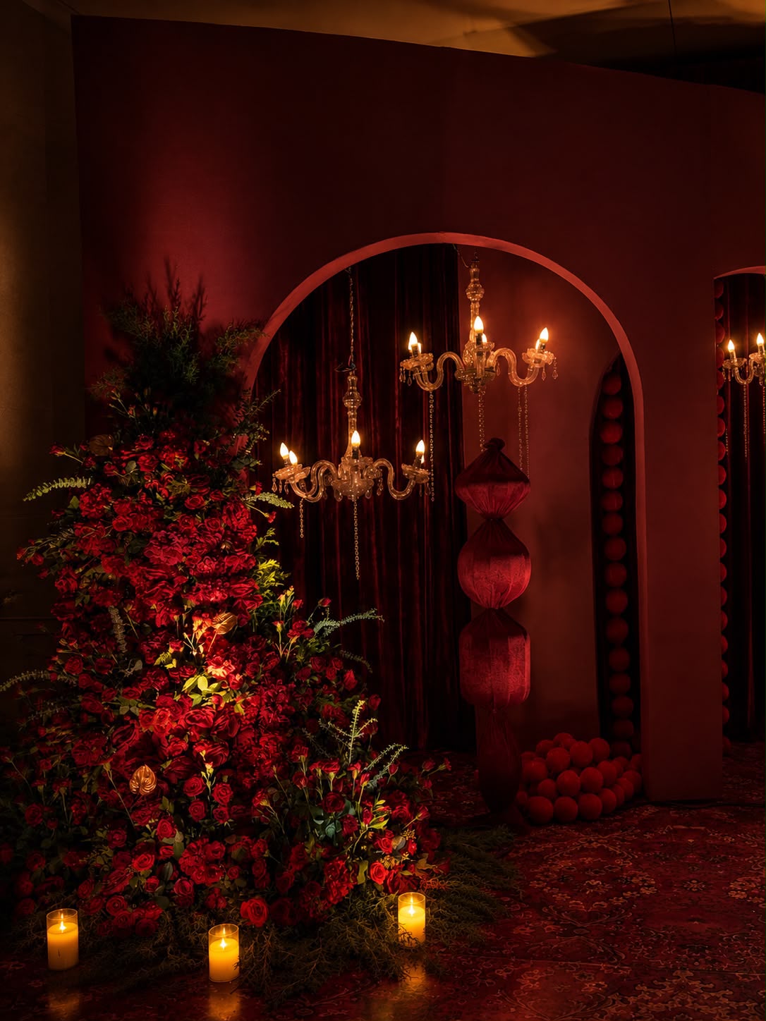 Red rose installation beside a chandelier-lit arch with velvet lantern column — Leela Palace Bangalore wedding decor by Panigrahana