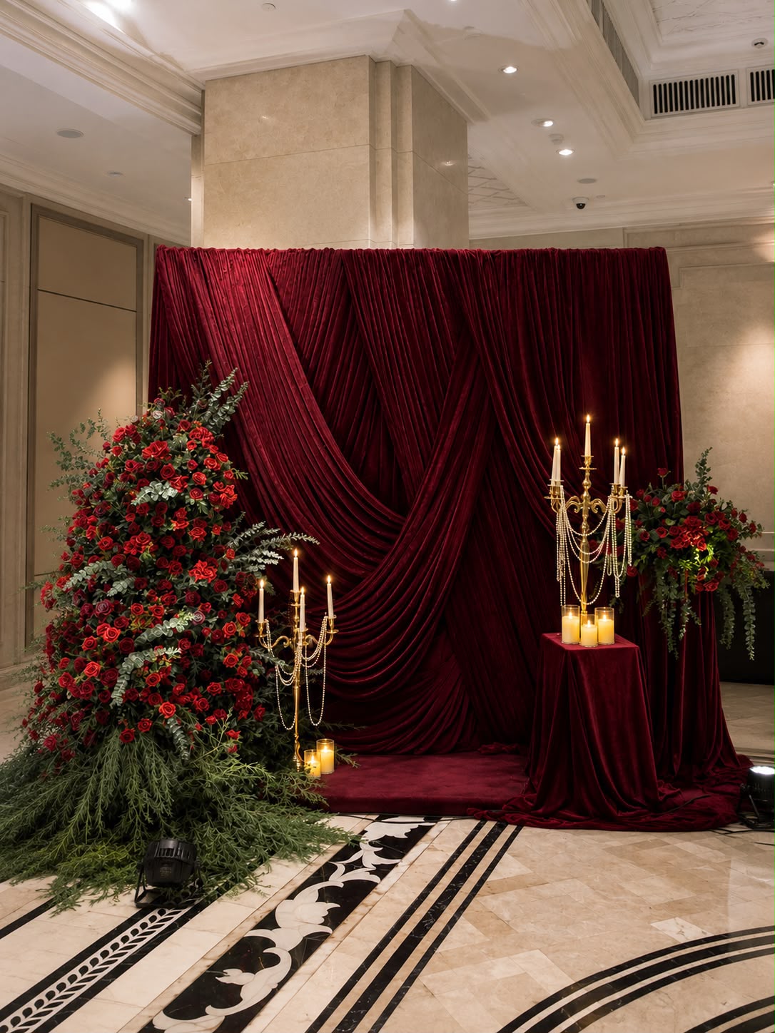 Burgundy velvet crossed-drape photo backdrop with candelabras and red roses on the marble floor at The Leela Palace Bengaluru
