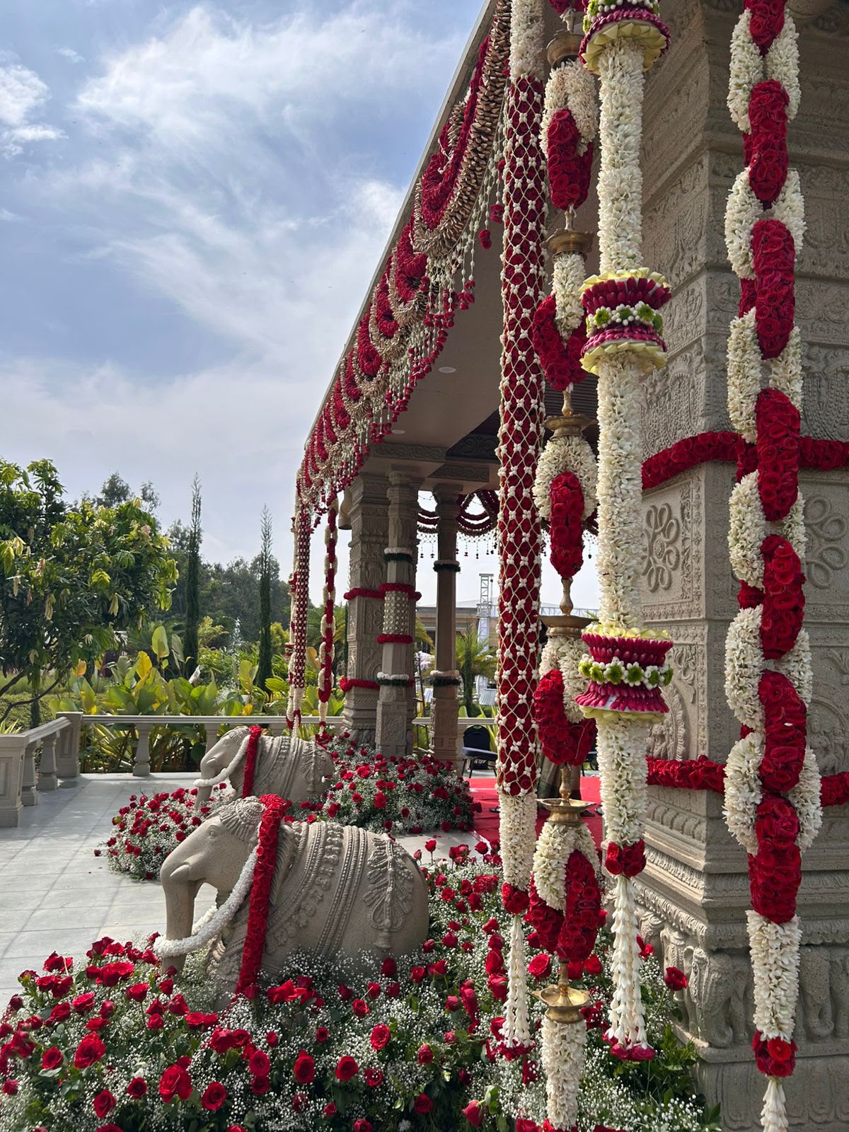 Stone elephants in beds of red roses beside carved pillars wrapped in tuberose and rose garlands at Utsavaa Bangalore