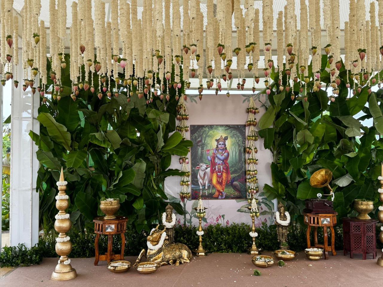 Krishna pooja corner with banana plants, tuberose and lotus bud strings, brass Nandi and gramophone at Utsavaa Bangalore