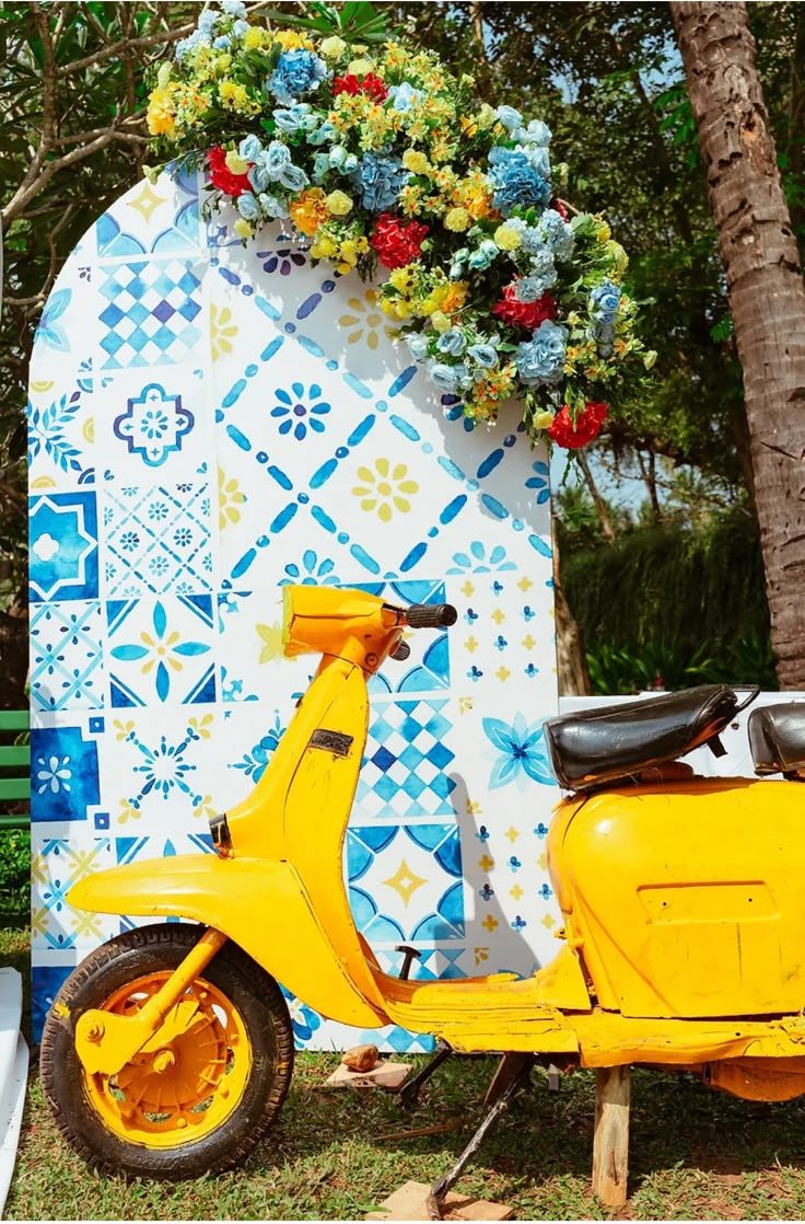 Yellow scooter parked against a blue and white azulejo tile arch topped with florals at the haldi