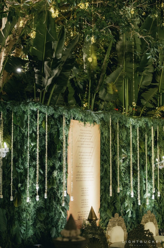 Close view of the greenery wall with jasmine strands and the parchment vows scroll under lit banana leaves at Nature Knots