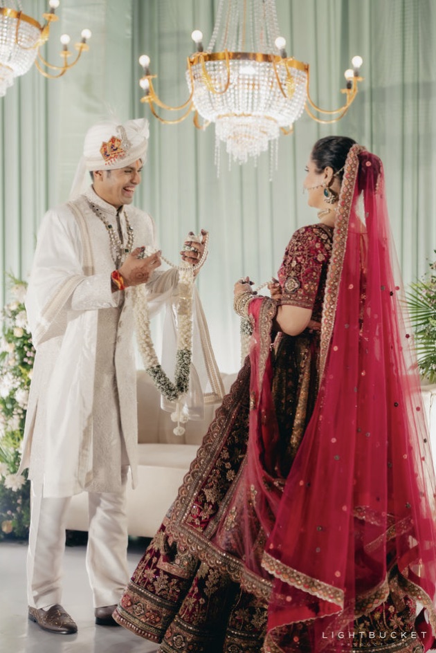 Couple exchanging jasmine jaimala garlands under crystal chandeliers against sage green drapes at Nature Knots Bangalore