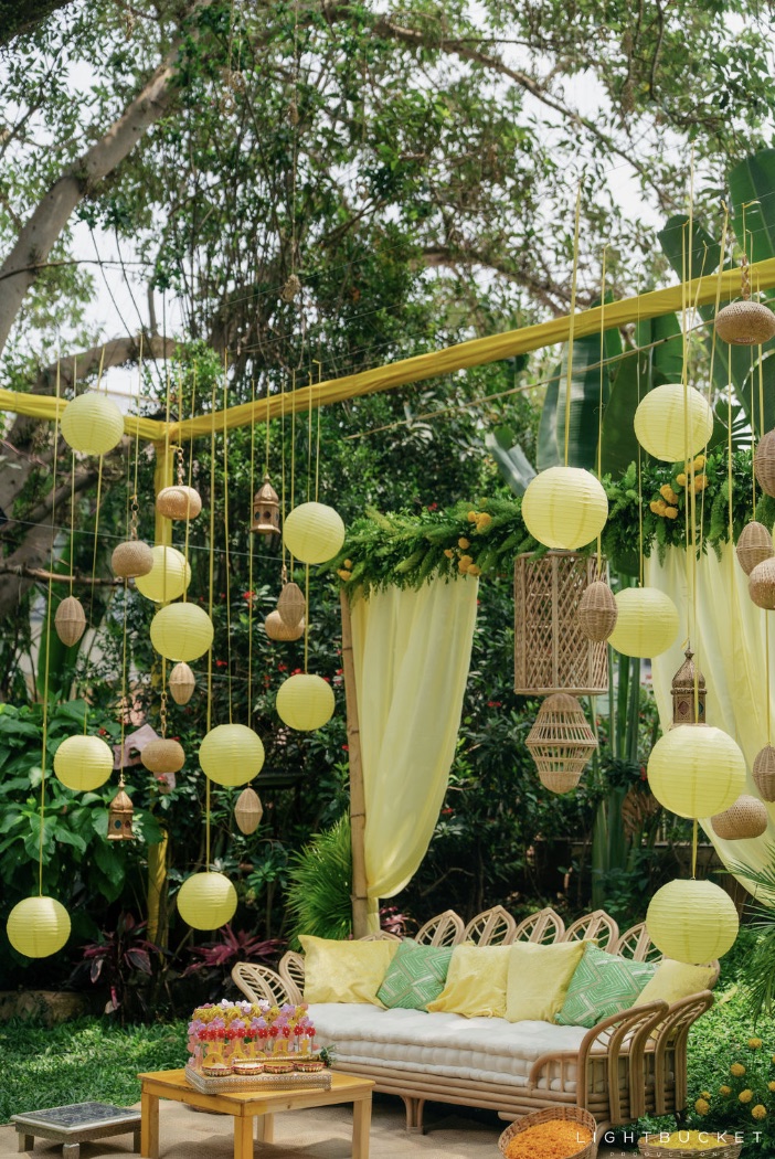 Haldi setup with lemon yellow paper lanterns and cane pendants over a cane sofa with yellow cushions at Nature Knots Bangalore