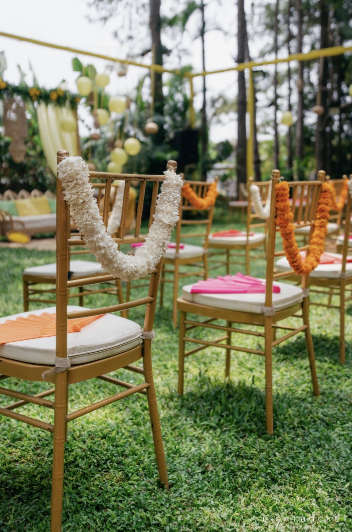 Gold chairs with white jasmine and orange marigold garlands and paper hand fans at a haldi in Bangalore