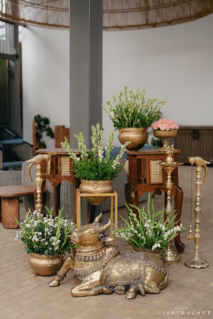 Brass Nandi with tuberose arrangements in gold pots on carved wooden tables at Nature Knots Bangalore