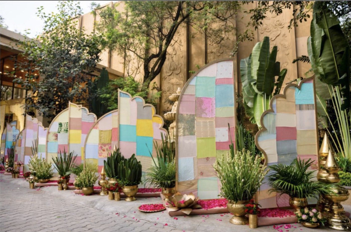 Row of scalloped patchwork screens in the courtyard at Chamara Vajra Bangalore with brass urns and live foliage