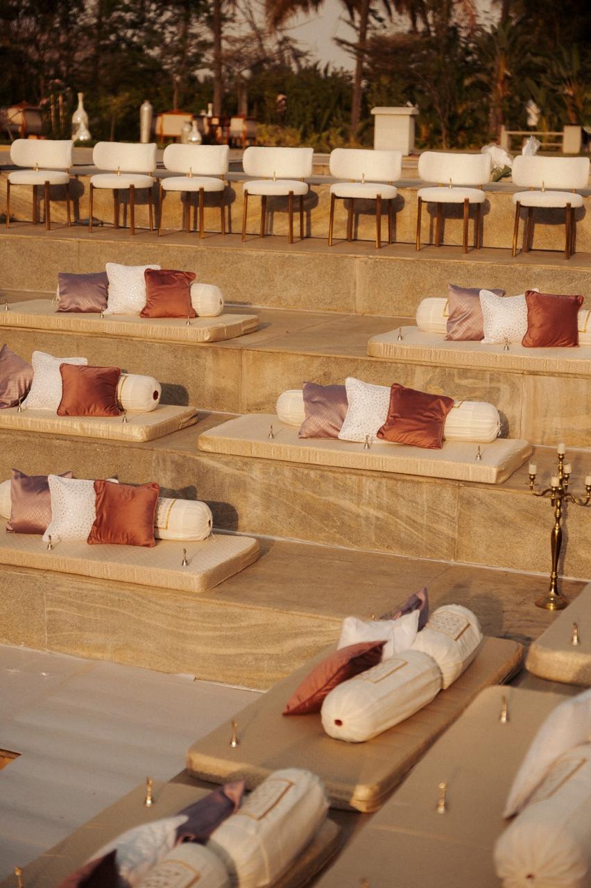Amphitheatre step seating with cream mattresses, bolster cushions in rose and mauve, and gold candelabra at Amita Rasa, Nandi Hills near Bangalore