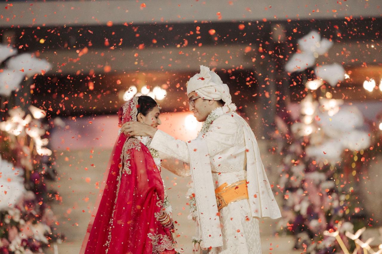 Groom garlanding the bride through a shower of rose petals at Amita Rasa, Nandi Hills near Bangalore