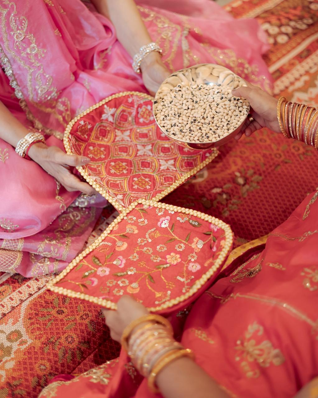 Pre-wedding ritual with a silver bowl of beans passed across embroidered red fans, women in pink and red
