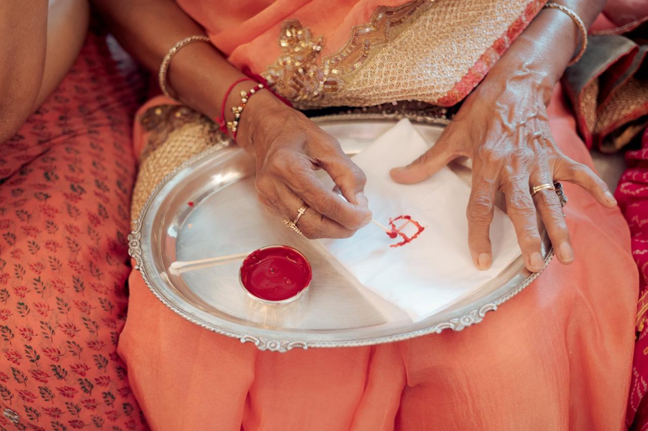 An elder writing a letter in red on white cloth on a silver tray during a wedding ritual