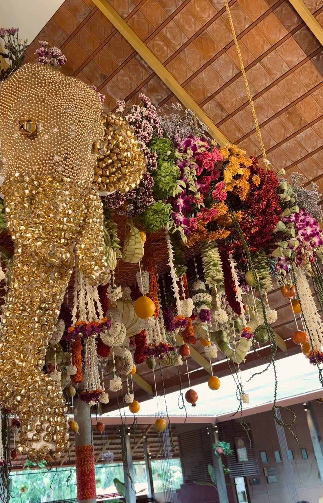 Detail of the suspended floral canopy at Panchavati Pavilion showing brass bells, pearl work, orchids, hydrangea, marigold, woven palm pendants and hanging citrus fruit