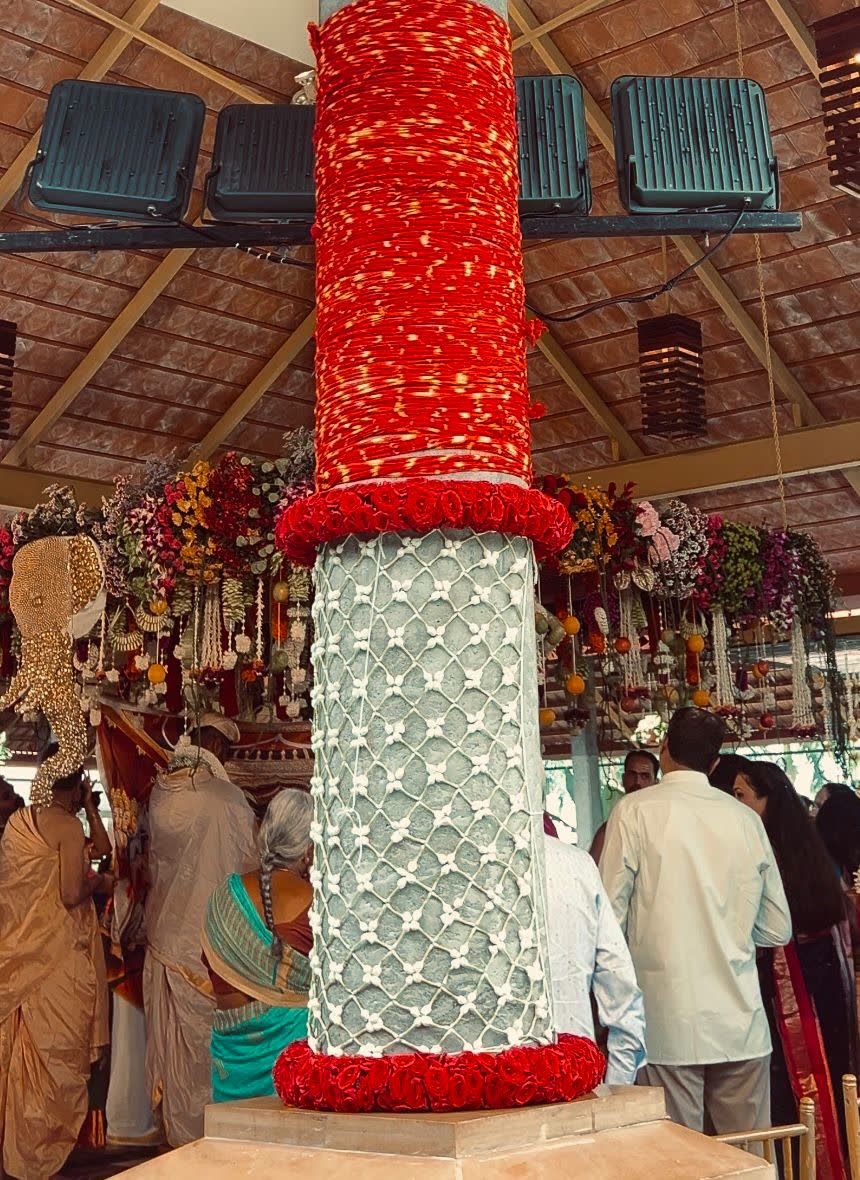 Mantap column wrapped in red rose garlands above and a white jaali net over stone below, banded top and bottom with rose rings