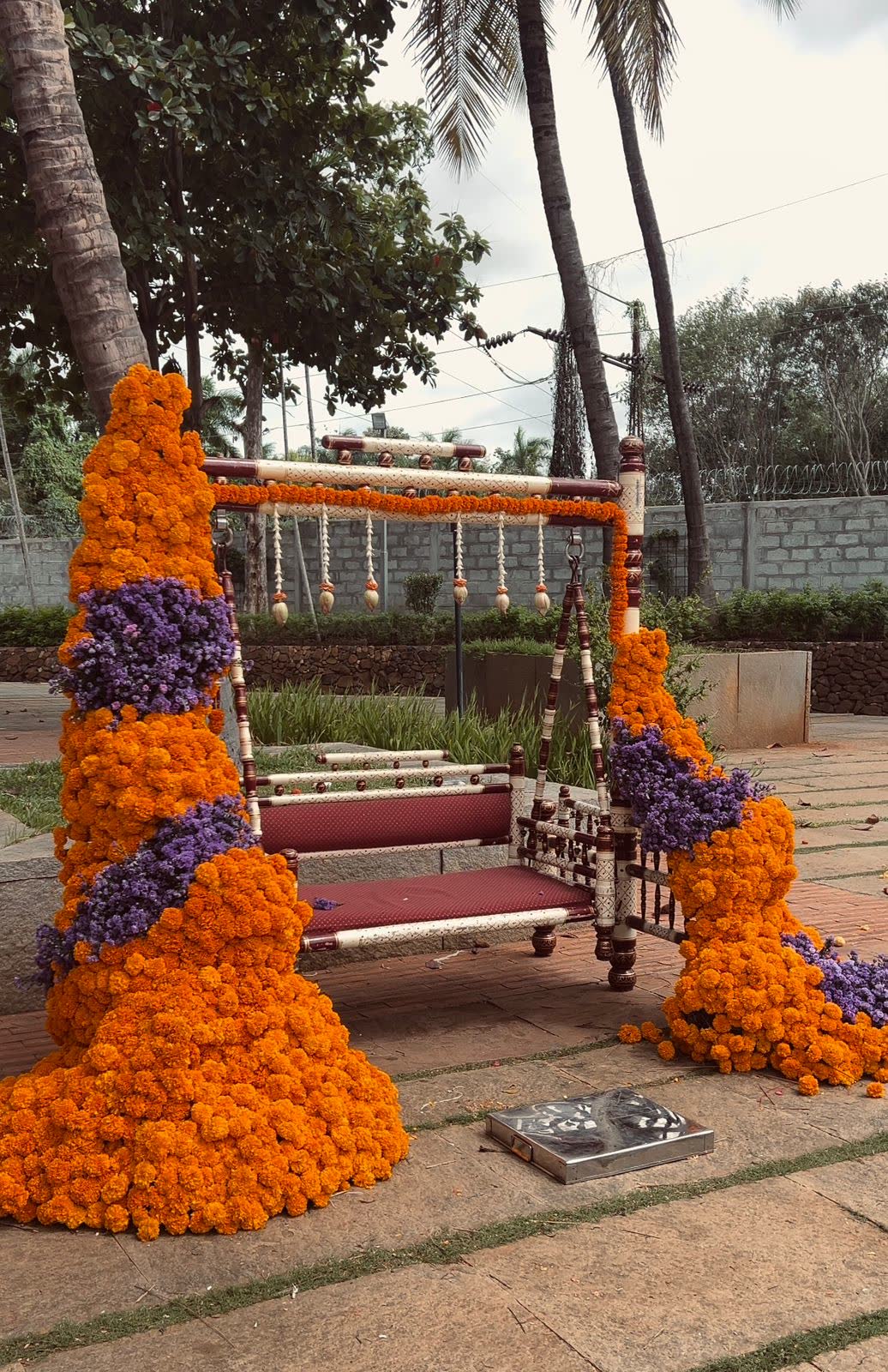 Side view of the marigold and statice wedding swing with hanging tassels and the lawn and coconut palms behind